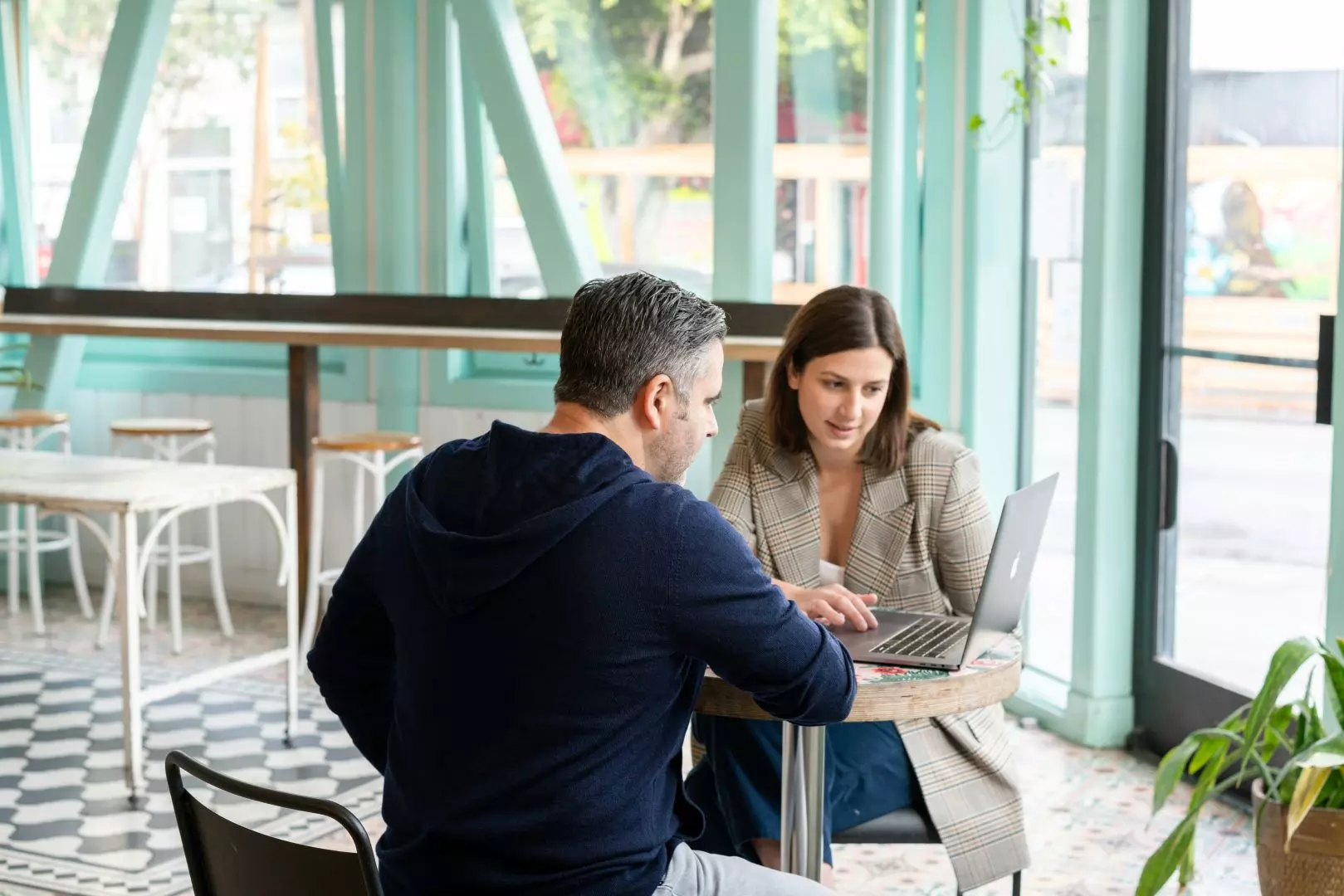 Dos personas reunidas en una cafetería trabajando en un ordenador portátil.